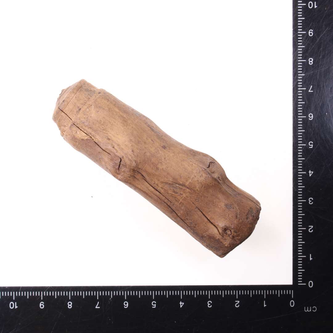 H�ndtag eller lignende af tr�, omtrentlig cylindrisk form
L�ngde:  7,8 cm
Knivsk�ret med kunsterne ikke bortsk�rne. I den ene ende spor efter, at genstanden har v�ret behandlet i drejeb�nk. Forarbejde.