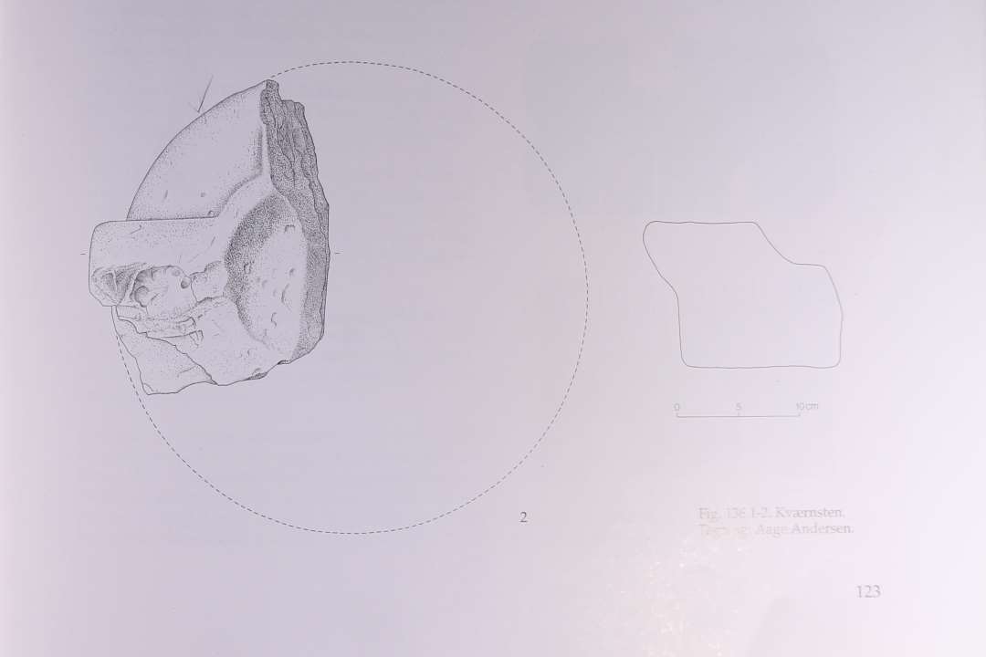 Fragment af flad, cylindrisk l�ber, hugget i por�s sandsten, som er lagdelt i gulliggr�t og violet. st�rste m�l er 19x12 cm., h�jden er 11,4 cm. P� oversiden er ved stenens midte en antydning af en lav, tragtformet �bning til indh�ldning af kornet bevaret. Fra denne forl�ber en oph�jet ribbe ud til stenens rand. I ribbens kant er en hugget fordybning, hvori et l�st drejeh�ndtag kan have v�ret placerert. Stnens underside og side er blankslidt.