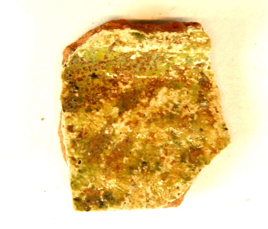 1 hals- skuldersk�r fra kande ? af r�dbr�ndt lergods med pibelersbegitning p� ydersiden, hvorover igen partiel r�dlersbegitning og gr�nligsp�ttet blyglasur. P� indersiden klar blyglasur, gruppe 1.