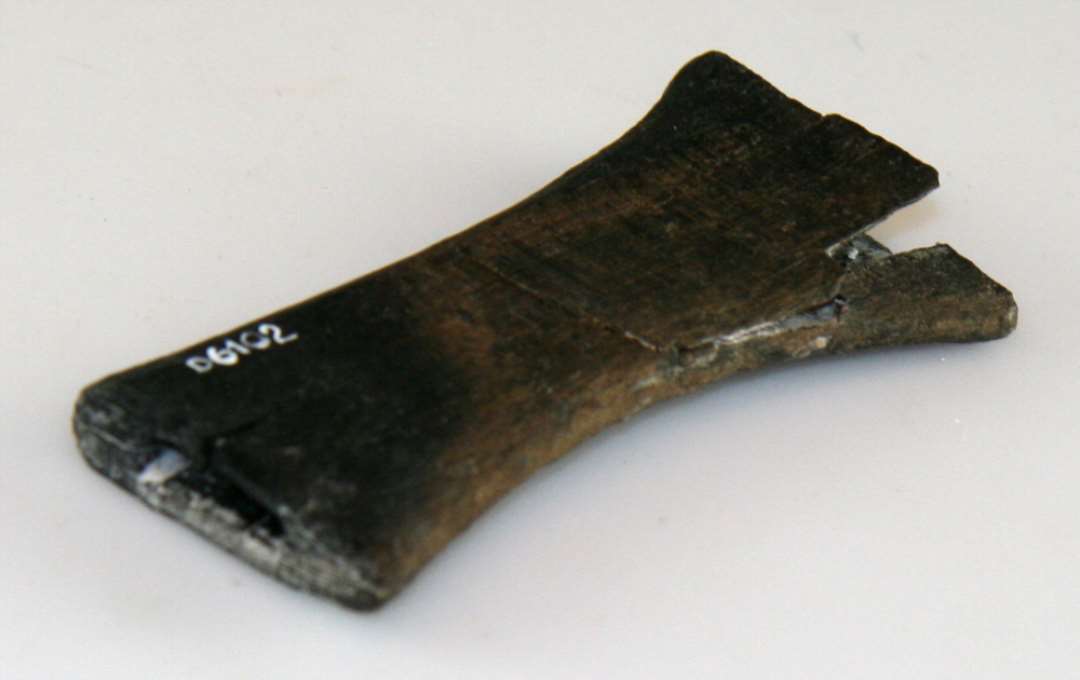 H�ndtag/skaft af b�getr�. Smallest p� midten, enderne udsvajede. Den ene ende udsparring til angel af jern eller lignende. L�ngde: 10,3 cm., bredeste stykke: 4,5 cm. tykkelse: ca 1 cm. En stump afbr�kket.