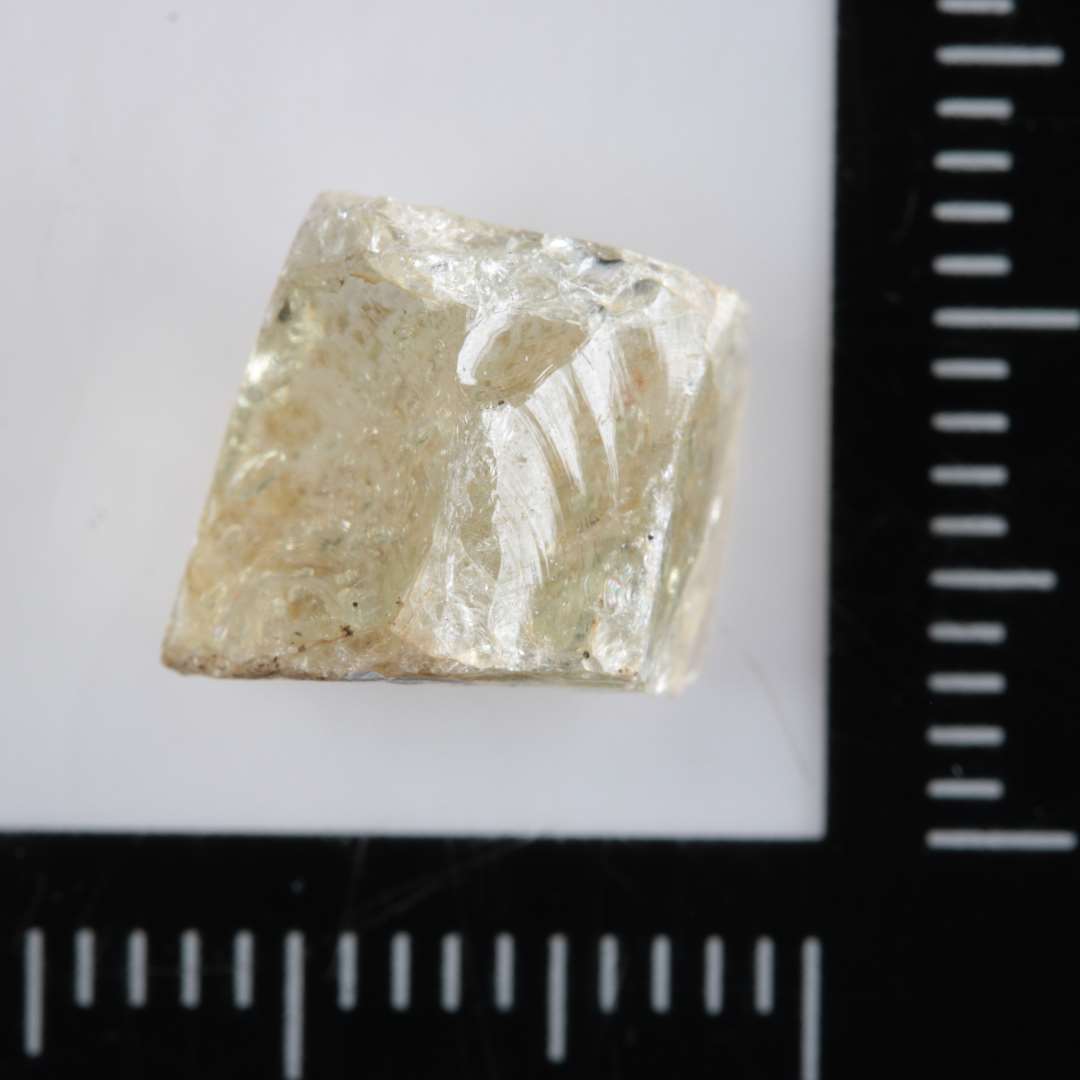 1 mosaikstift af uregelm�ssig kubisk form og af hvidt gennemsigtigt glas med rester af guldfoliebel�gning p� den ene side.�