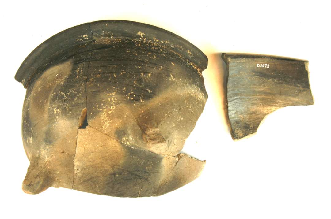 Et randsk�r samt 1 parti  ( ca. 1/4 ) af lavt grydeformet kar af brunt og gr�sort flammet jydepottegods samlet af flere sk�r. Karfragmentet udviser to korte knivbesk�rne t�er af tilspidset form. Korpus har kuglekaltagtig form uden halsmarkering og afsluttes foroven med en vandret fremst�ende mundingskrave. Ydersiden fremviser enkelte glittestriber, indersiden er helt blankglittet i stribet form. Karh�jde ca. 11 cm. St�rste randdiam. ca. 23,5 cm.