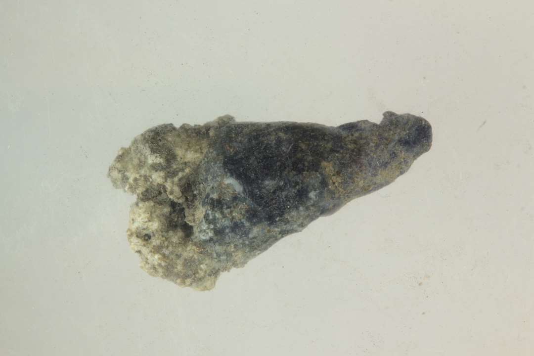 1 kr�mmerhusformet stump smeltet glas af bl�ligt gennemsigtig glasmasse i hvis brede ende er fastsmeltet en stump sintret lerslagge.�L�ngde: 1,9 cm.