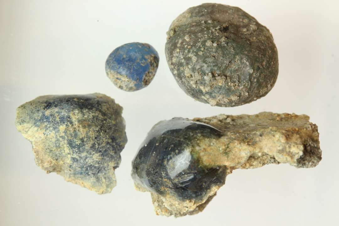 4 klumper smeltet bl�t, gennemsigtigt glas med sintringsskorpe, is�r p� den ene, varierende fra peberkorn- til stor �rtest�rrelse.