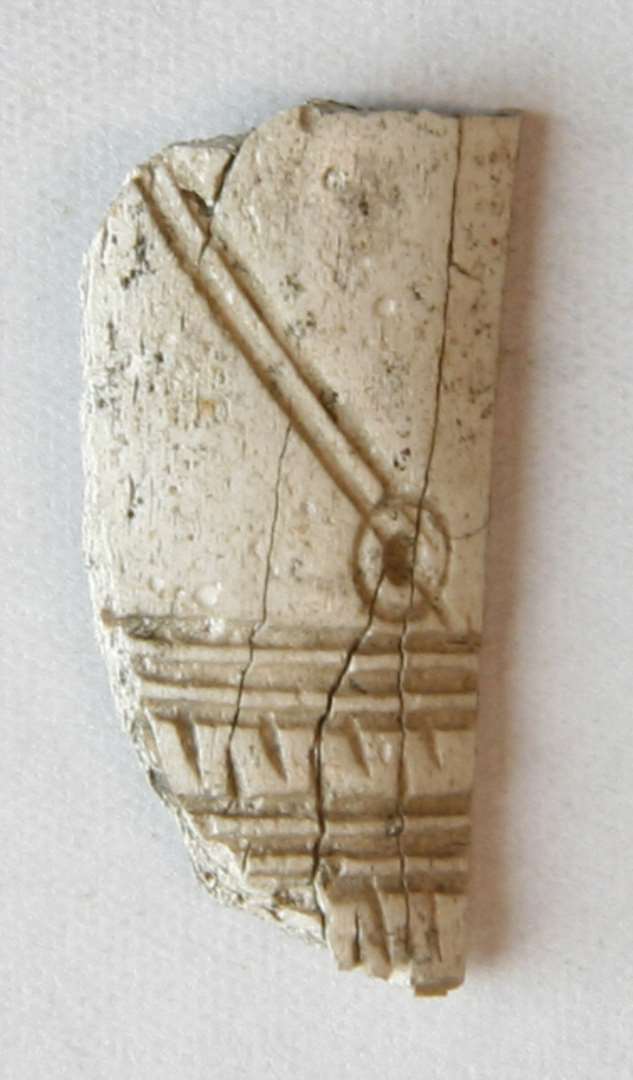 1 hvidbr�ndt fragment af kamskinne af hjortetak med stregornamentik og et cirkelsalg.�L�ngde: 2,2 cm.