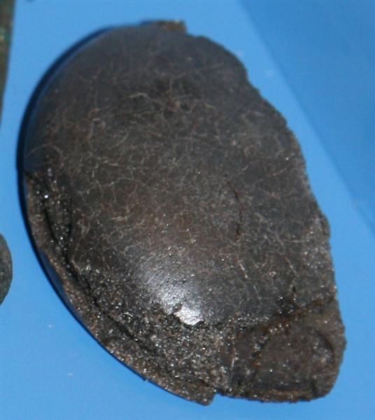 Fragment af cirkul�r glittesten/s�mglatter af ugennemsigtigt forvitret gr�nligt glas. Fragmentet udg�r ca. halvdelen af glittestenen, der har form af en kuglekalot med kraftigt afrundede kanter og opadhv�lvet uj�vn underside.  St�rste bevarede l�ngde og bredde: ca. 6,6 x 4 cm.  St�rste h�jde: 2,5 cm. Stenens oprindelige diameter kan beregnes til ca. 7 cm.