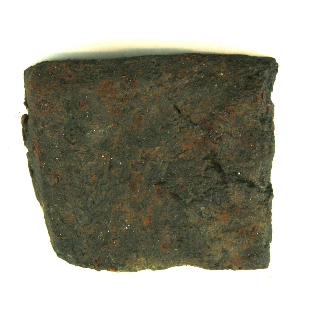 Flad jernbarre af lidt uregelm�ssig, rektangul�r form ca. 7,6 x 9 cm. Barren er omtrent plan p� den ene side, men noget konkavt formet p� den modst�ende side, ligesom dens ene hj�rneparti er betragtelig tykkere end de andre. Tykkelsen svinger derfor fra 1,3 cm. til 2,3 cm.