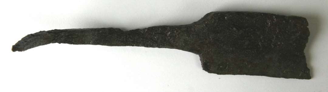 1 fragmenteret blad med secund�rt krumb�jet skafttunge fra dolk eller daggert. Bladet har tresidet tv�rsnitsform og er skr�t overbrudt ca. 5 cm. fra skafttungen, der ligger fors�nket b�de i forhold til den brede bladryg og til bladundersiden, sidstn�vnte har ikke karakter af en skarp �g, men af en smal stump kant. Fragmentets nuv�rende l�ngde 13,8 cm., heraf udg�r bladet ca. 5 cm. I udrettet stand m�ler skafttungen ca. 12 cm. Bladets bredde: 3,2 cm. Bladets st�rste tykkelse ved bladryggen: 0,5 cm.