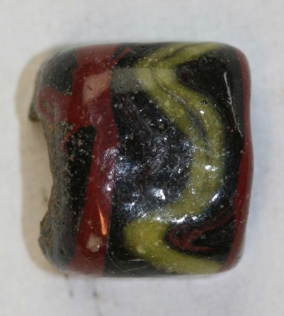 Kubisk, cylindrisk, halv, uigennemsigtig, sort med r�de b�nd og gule zigzagger. St�rste m�l: 1 cm.