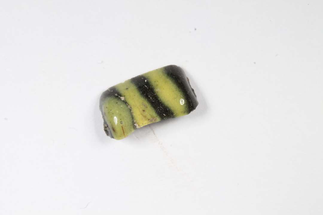 Fragment af cylindrisk, uigennemsigtig glasperle. Sort med gult, ligner Hvepseperle, men gule tr�de er ikke�lagt p� s�dvanligvis. Se ogs� x177. St�rste m�l: 1 cm.