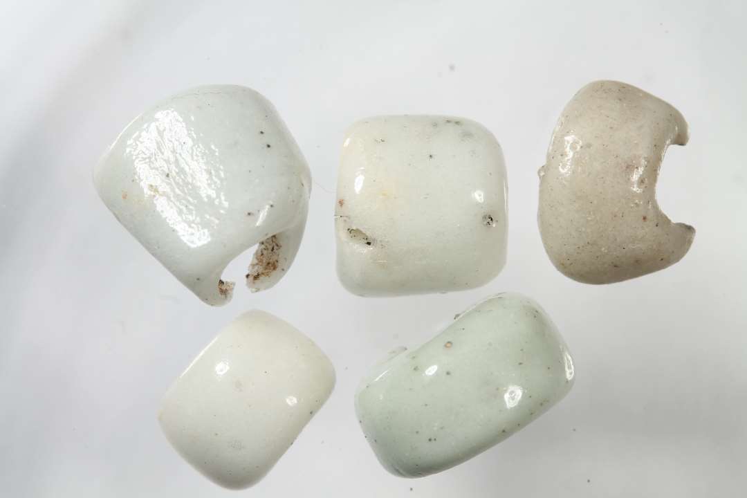 Fem halve cylindriske, uigennemsigtige, hvidgr� glasperler. Diameter: ca 0,7-1 cm.