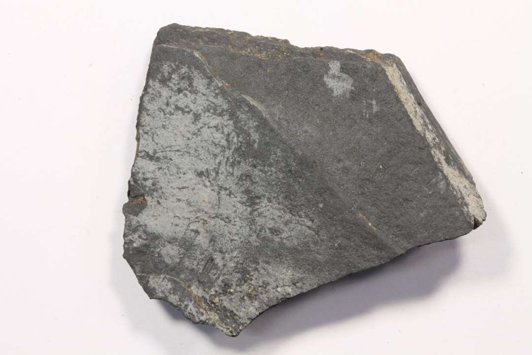 Fragment af hv�ssesten af sort, finkornet skifer. Uden slibespor. m�l: 4,5 cm.