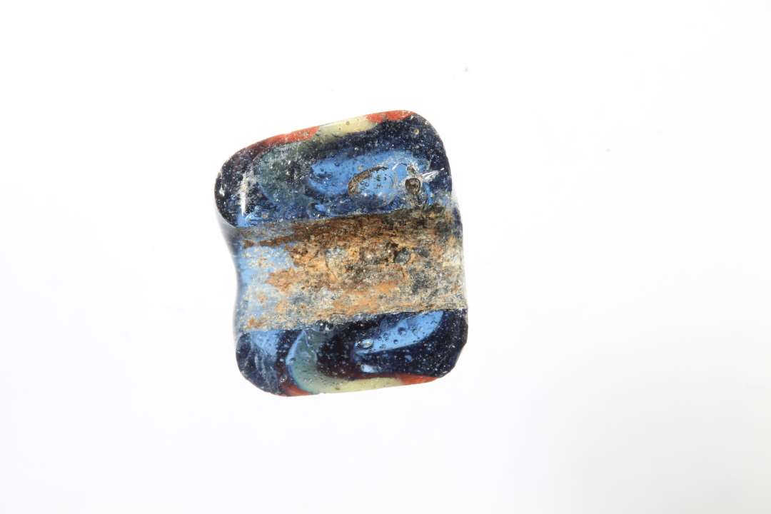 Fragment af cylindrisk ribeperle, gennemsigtig bl� med r�dt og gult. diameter: 1,1 cm.