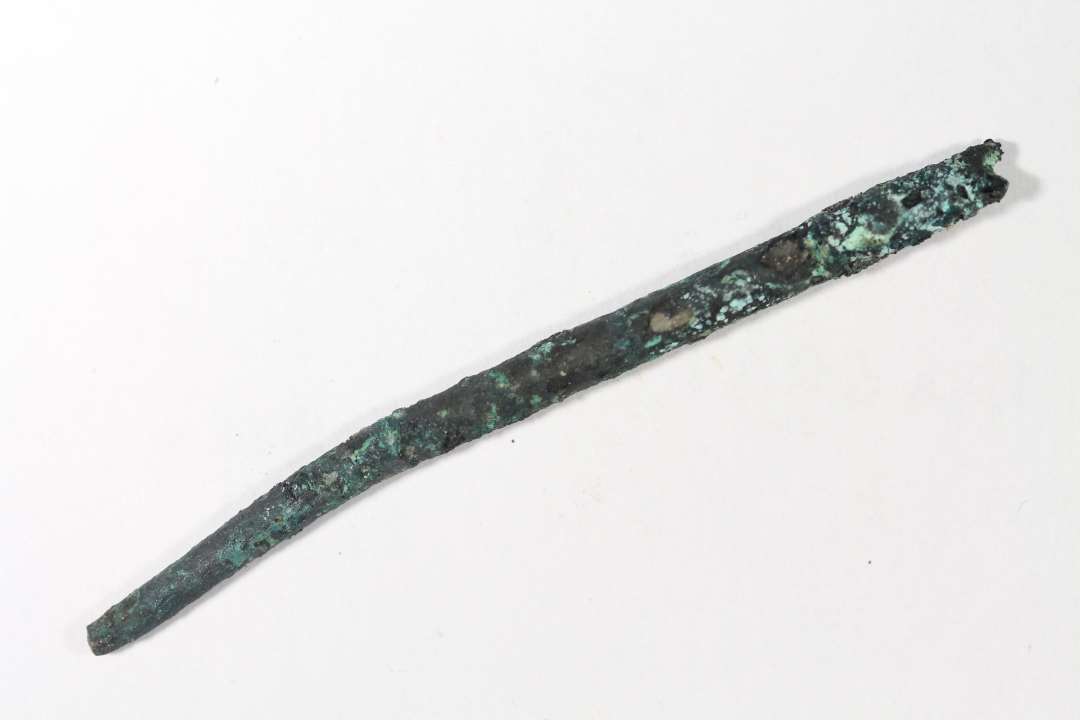 Fragment af bronzen�l. Afbrudt spids. L�ngde: 5,6 cm. Delvist bevaret �je, herunder profilering. D�rligt bevaret.