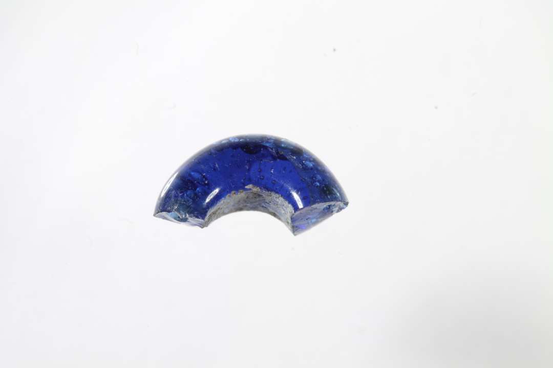 Halv ringformet, gennemsigtig bl� glasperle. Diameter: 1,1 cm.