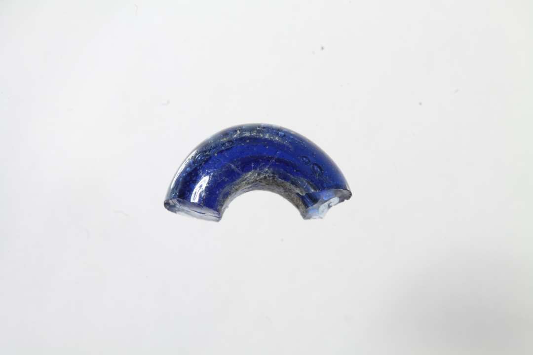 Halv ringformet, gennemsigtig bl� glasperle. Diameter: 1,1 cm.