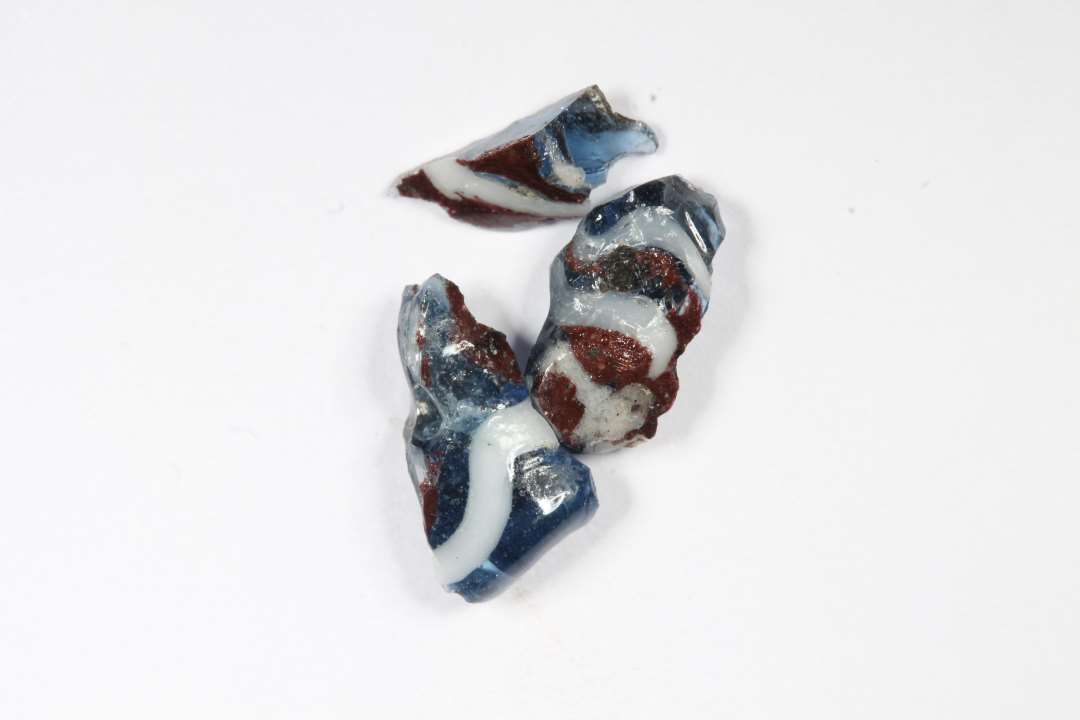 Tre fragmenter af cylindriske ribeperler. Gennemsigtige, bl� med r�dt og hvidt. St�rste m�l: 0,7-1 cm.