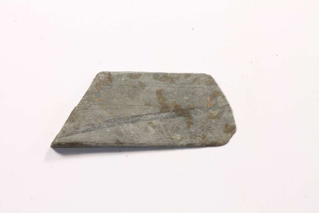 Fragment af hv�ssesten af lysegr� skifer. M�l: 1,4x0,5x3,5 cm.