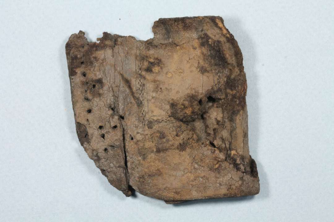 Kraftigt l�der, der er bukket og�har v�ret syet sammen langs den�ene side. Indstemplet m�nster og�linier p� den ene side. Fragmenteret.