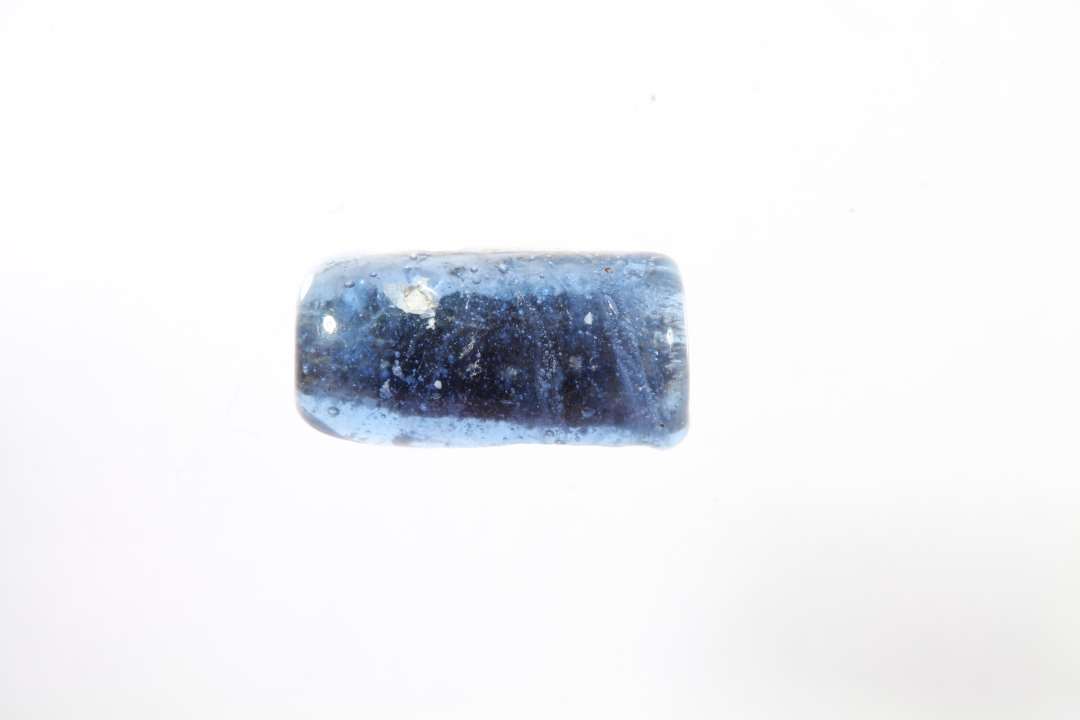 Halv cylindrisk, gennemsigtig bl� glasperle. L�ngde: 1,1 cm.