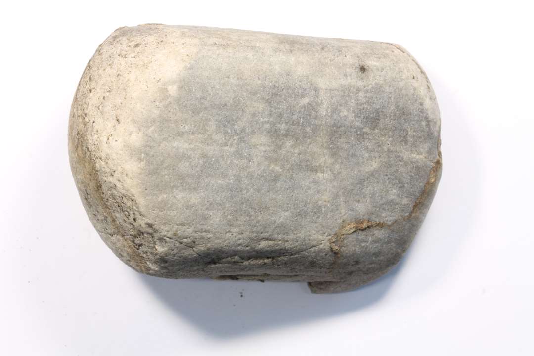 Knusesten af lys, gr� granit. Tydelige knusem�rker i omr�derne ved de to ender. M�l: 5,3x4,4x8,2 cm.