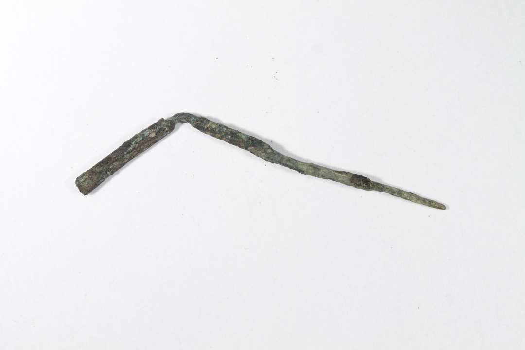 Fragment af bronzen�l. Svagt kr�mmerhusformet, massiv bronzegenstand, b�jet. L�ngde: 4,5 cm.