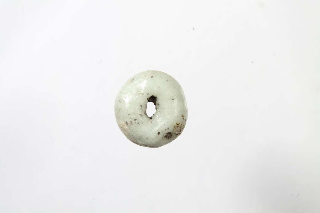 Ringformet, uigennemsigtig, hvidgr� glasperle. Diameter: 0,8 cm.
