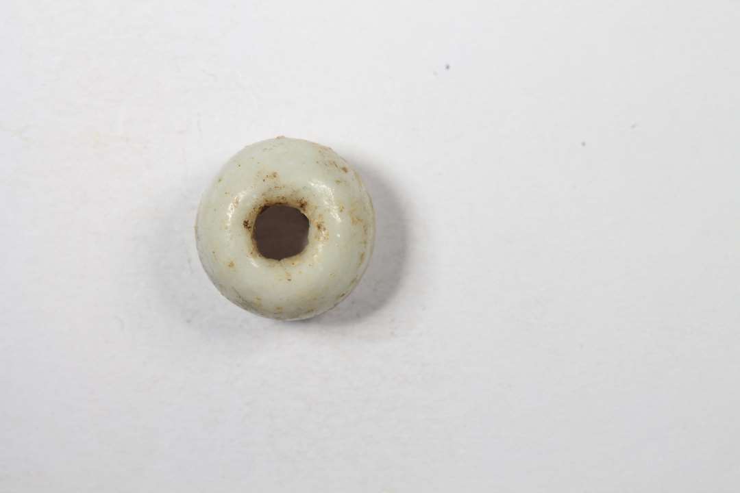 Ringformet, uigennemsigtig, hvidgr� glasperle. Diameter: 0,7 cm.