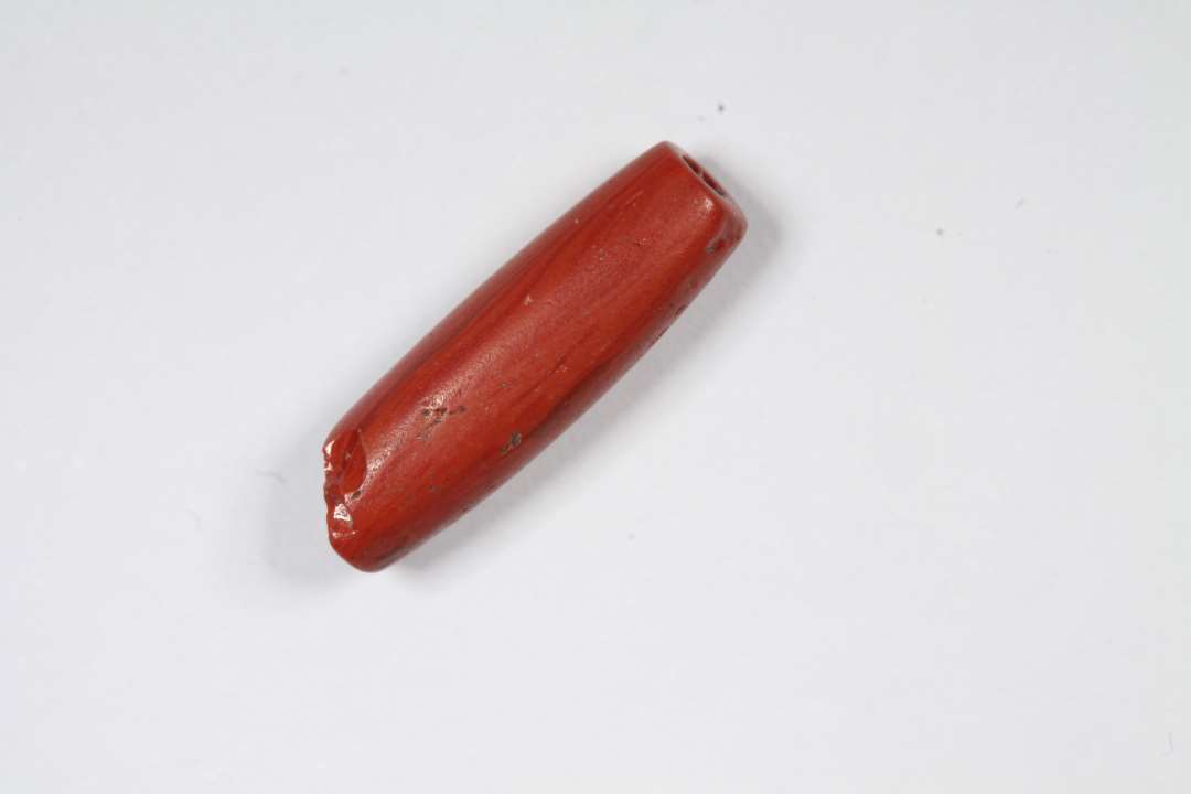 Cylindrisk, uigennemsigtig, r�d glasperle. Lang og tynd, r�rformet. L�ngde: 1,4 cm.