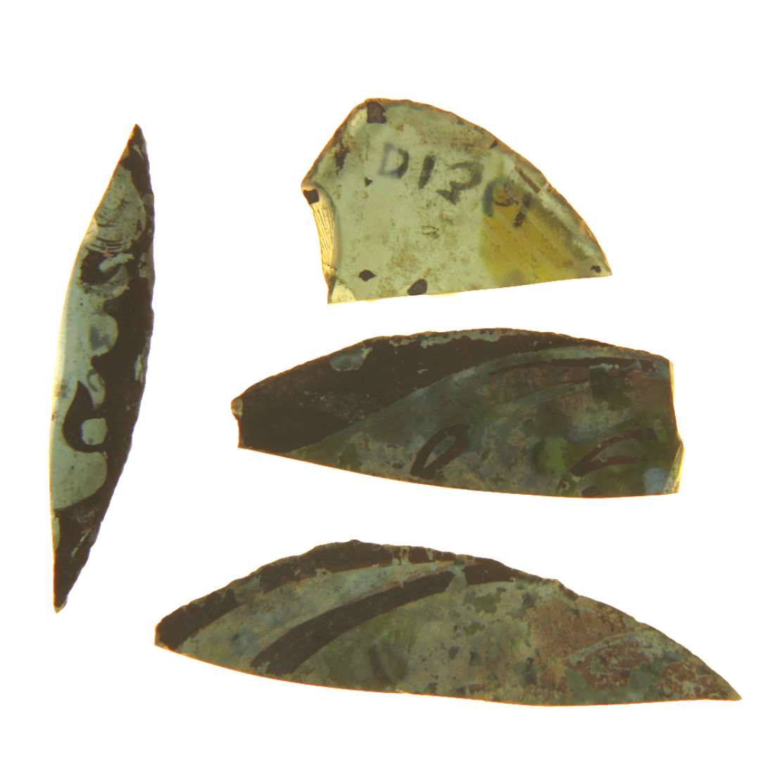 4 fragmenter af ruder i bl�t glas med afnappede kanter, hvoraf de 3 er bemalet med stregornament i brune og gule farver, det fjerde udviser en stump af et stiliseret blomstermotiv p� brunmalet baggrund. Hidr�rer antagelig fra ruder af hel- eller halv- eller delvis cirkul�r form.�St�rste m�l: 1,9 x 2,6 cm. - 1,5 x 4,2 cm. - 1,35 x 5,35 cm. - 0,9 x 4,5 cm.