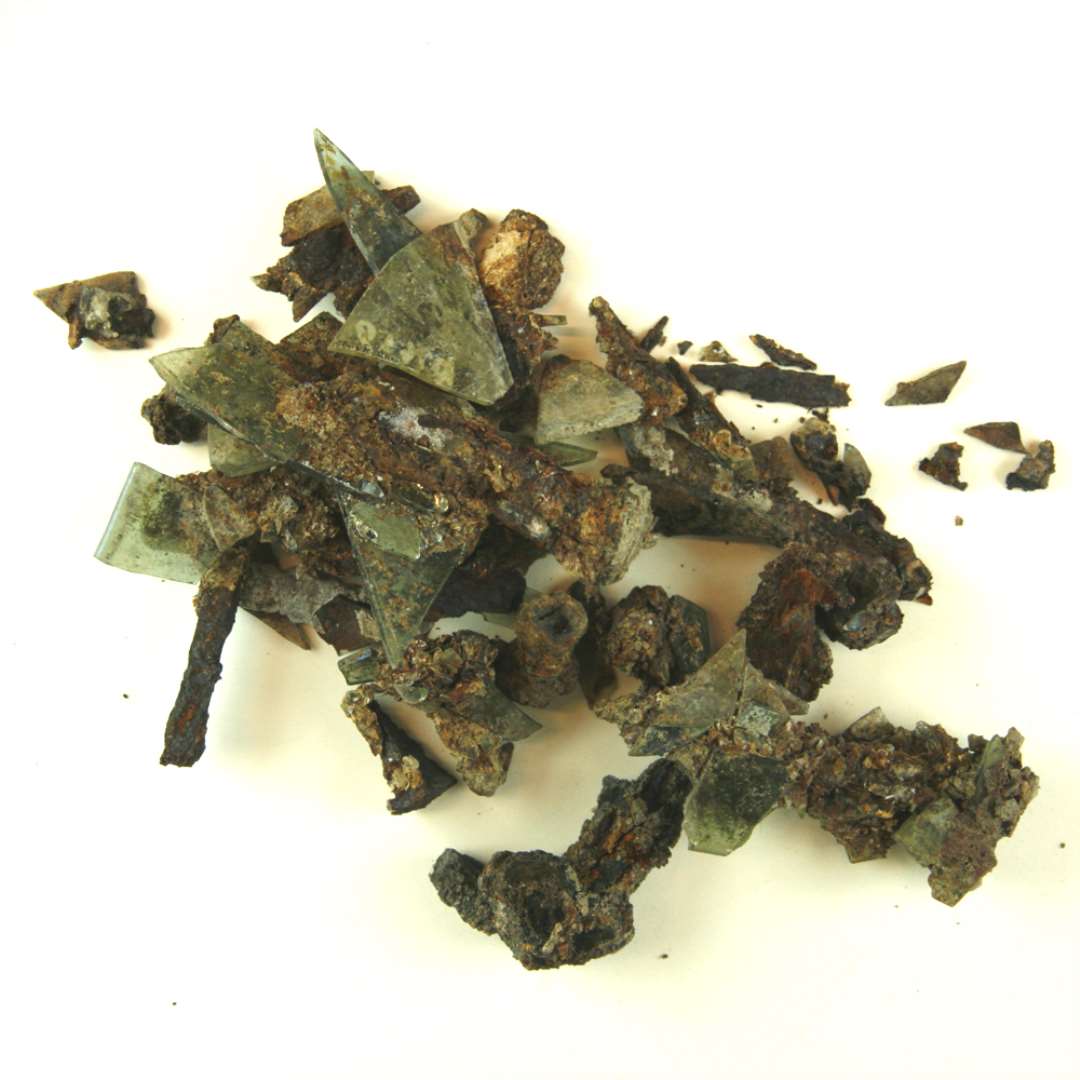 1 samling st�rkt forrustet jerns�m i hvis rustlag er fastkittet talrige sk�r af klart gr�nligt glas, af de fleste uden spor af forarbejdning, enkelte med afnapning i kanten.