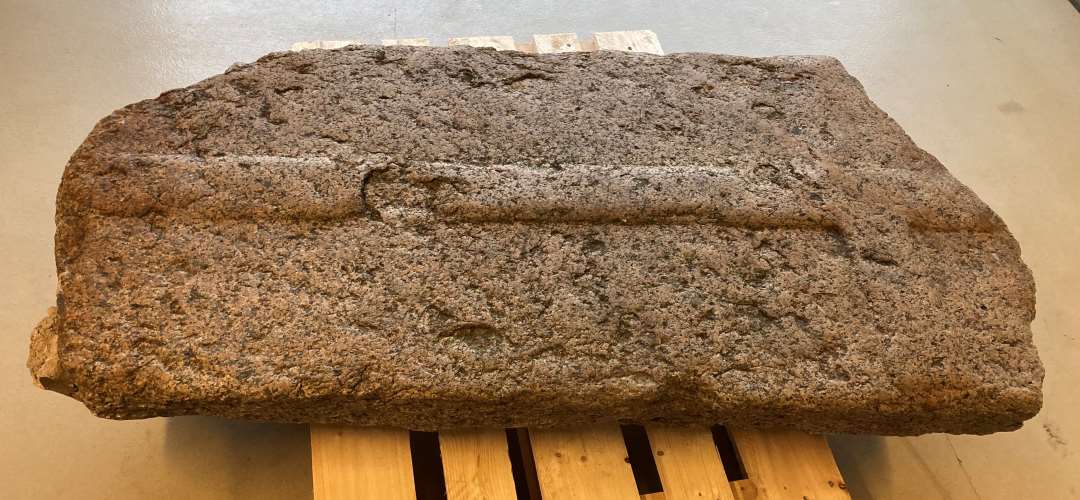 Gravsten af grovkornet, gr� granit med reliefhugget kors, �verste del af stenen mangler. H�jde: 154 cm. Bredde: 79 cm. Tykkelse:  20 cm.  