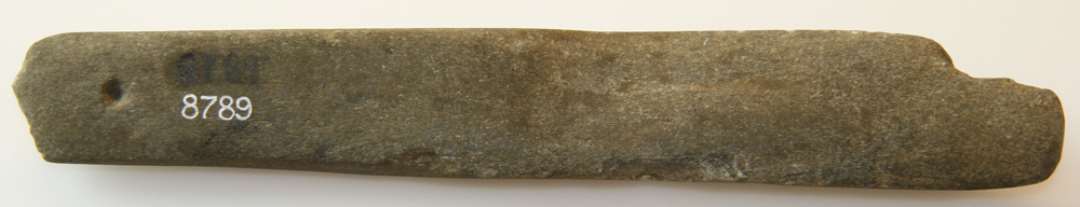 Hv�ssesten. Aflang, en flis mangler i begge ender. P�begyndt boring af hul fra den ene side i den smalle ende. L�ngde: 17,5 cm., bredde: 2,1/2,7 cm.