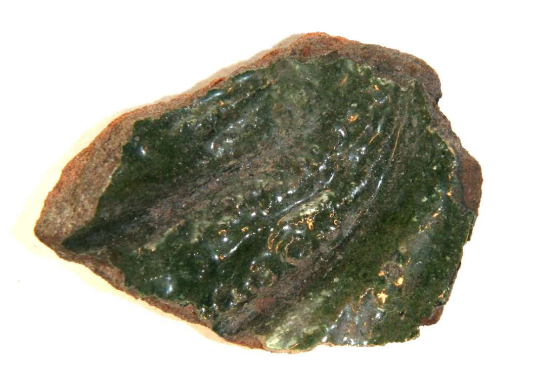 Fragment fra midterpartiet af gr�nglaseret kakkel. P� forsiden ses del af krum, hornlignende genstand med t�tsiddende ringvulster af nipsen�lshoveds st�rrelse. St�rste m�l: 5,5 cm.