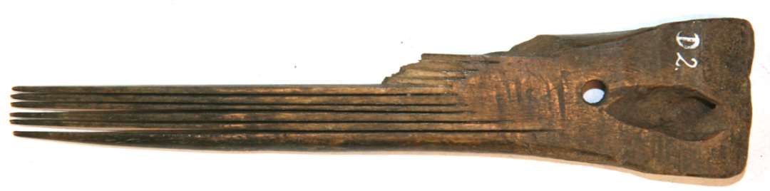 Langtandskam. Af udsavet ben. L. 15,5. st. br. 3,2. 11 t�nder, hvoraf de 5 er kn�kket af. Gennemboring i hovedet.